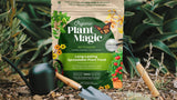 Bag of all purpose fertilizer granules with a leafy backdrop surrounded by gardening tools including a watering can, trowel, and fork.